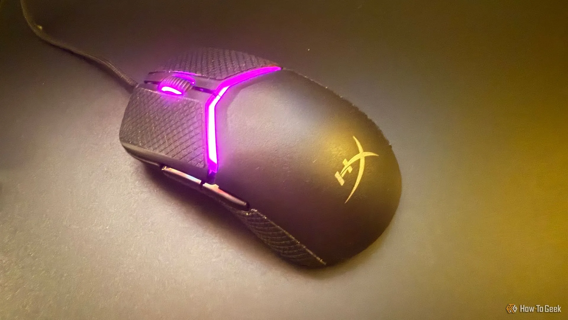 Chuột HyperX Pulsefire Saga trượt mượt mà trên bàn di chuột thủy tinh, thể hiện dây cáp linh hoạt và feet chuột tối ưu.
