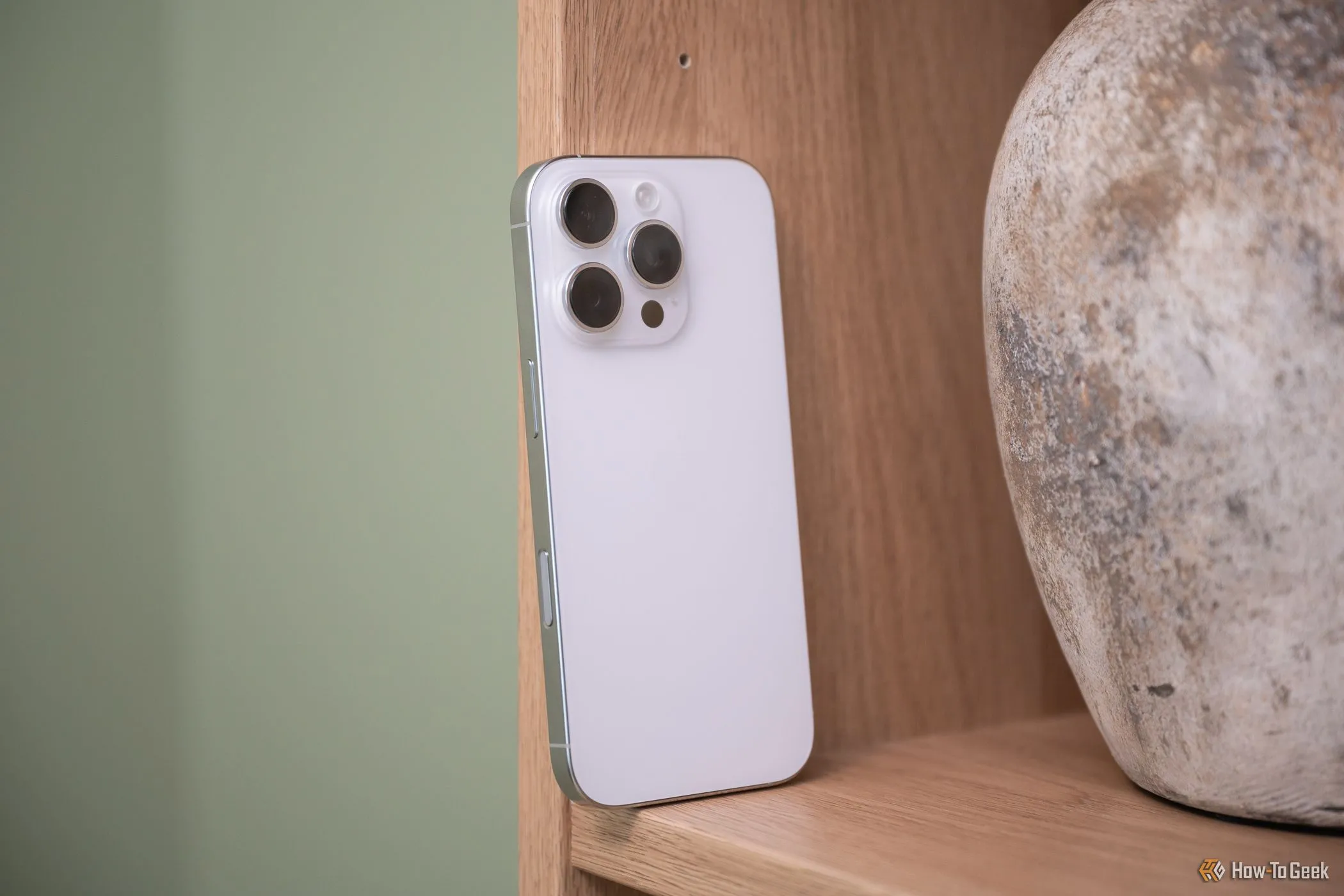 Điện thoại iPhone 16 Pro màu đen với nút điều khiển camera mới, đặt trên giá sách.