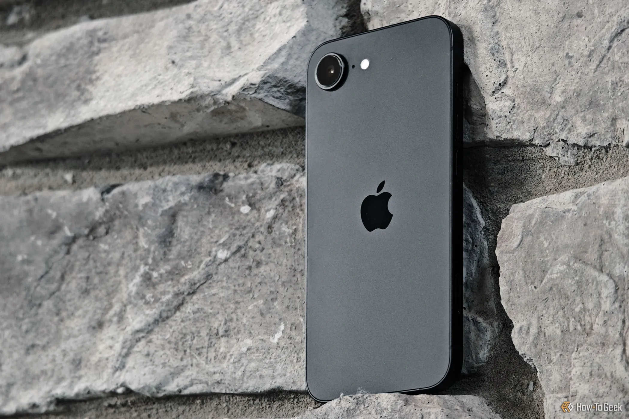 Điện thoại iPhone 16e đặt trên nền tường gạch, minh họa thiết kế camera.