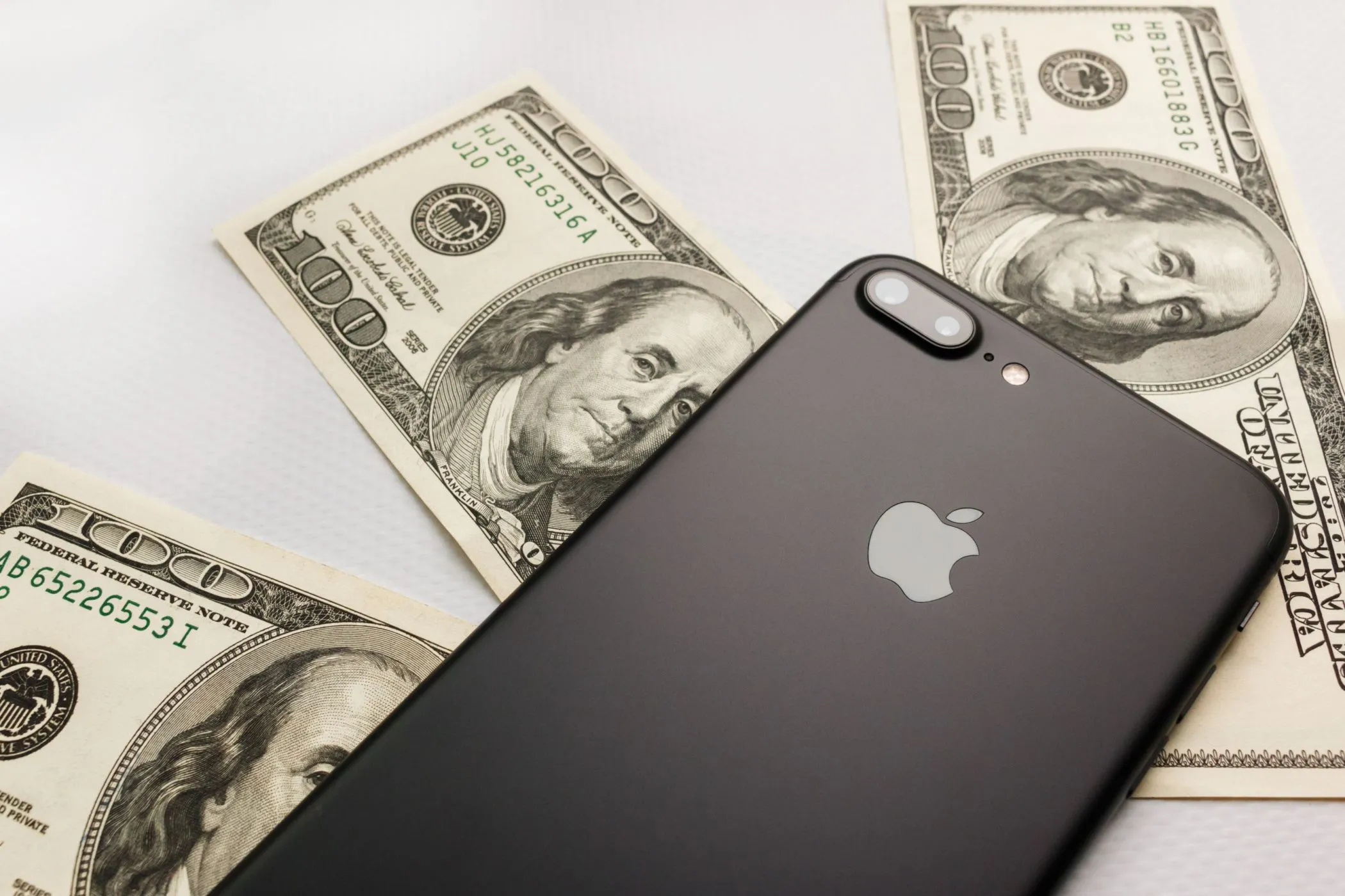 Điện thoại iPhone 8 Plus màu đen đặt trên cọc tiền ba trăm đô la, minh họa chi phí không kiểm soát khi chơi game gacha.