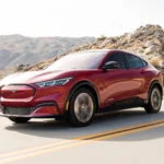 Mẫu xe Ford Mustang Mach-E màu đỏ 2021 di chuyển trên đường nông thôn, minh họa dòng xe bị triệu hồi lỗi cửa.