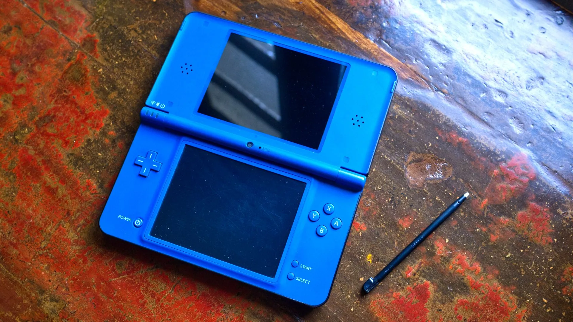 máy chơi game cầm tay Nintendo DSi XL màu xanh dương mở ra với bút cảm ứng, hiển thị rõ màn hình kép và khả năng chạm