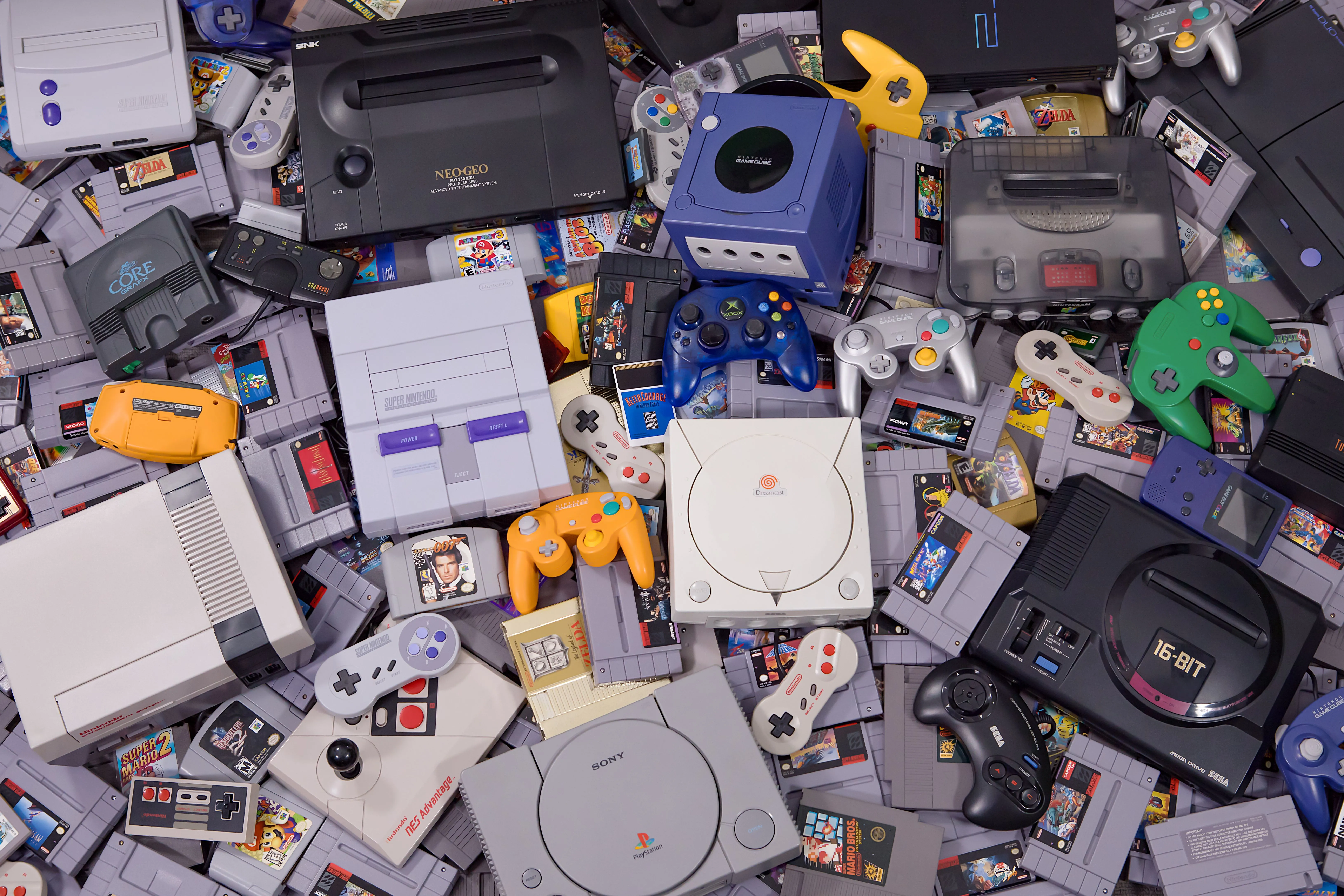 Một cảnh studio với nhiều hệ máy chơi game, tay cầm và băng game cũ như NES, PlayStation, minh họa cho game retro.
