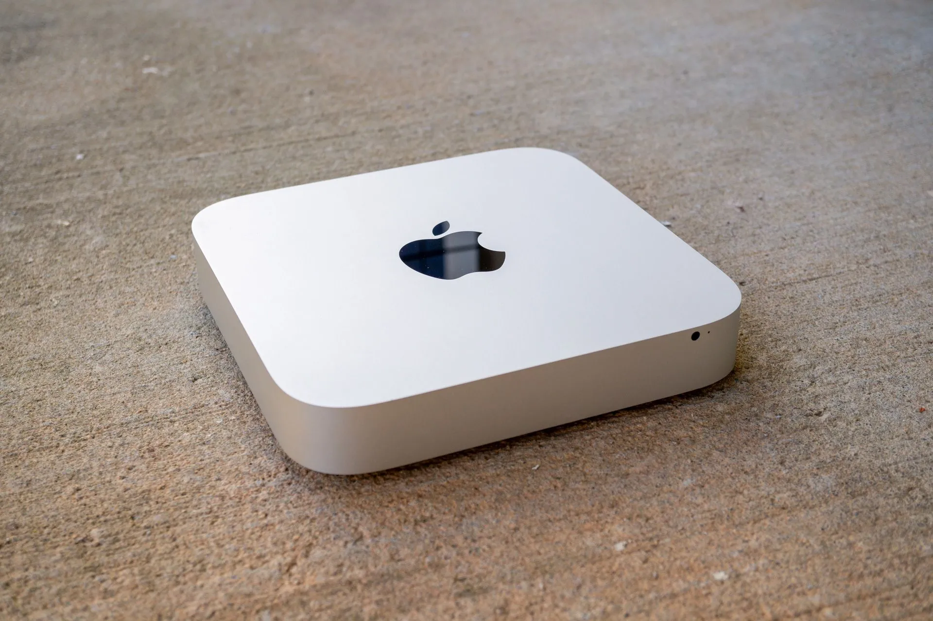 Một chiếc máy tính Mac Mini đặt trên bề mặt bê tông, thể hiện sự nhỏ gọn và thiết kế đặc trưng của sản phẩm Apple.