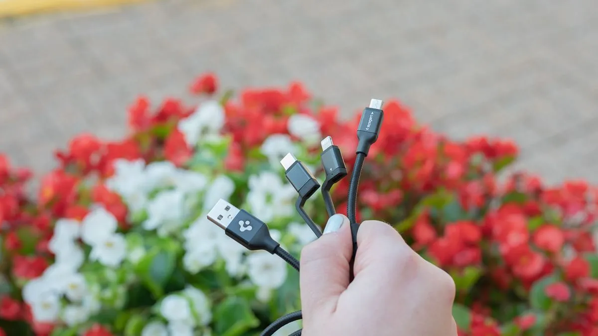 Người dùng cầm cáp sạc đa năng Spigen DuraSync 3 trong 1 với các đầu nối USB-C, Lightning, Micro-USB.