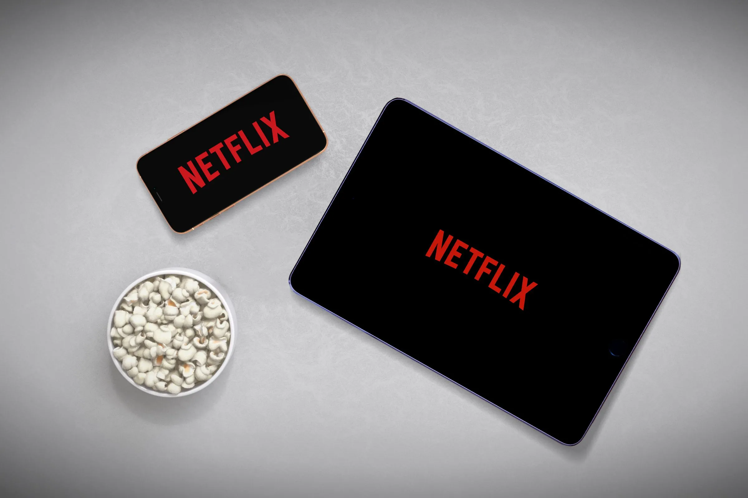 So sánh trải nghiệm xem phim Netflix trên màn hình điện thoại và máy tính bảng lớn hơn, với tô bỏng ngô bên cạnh