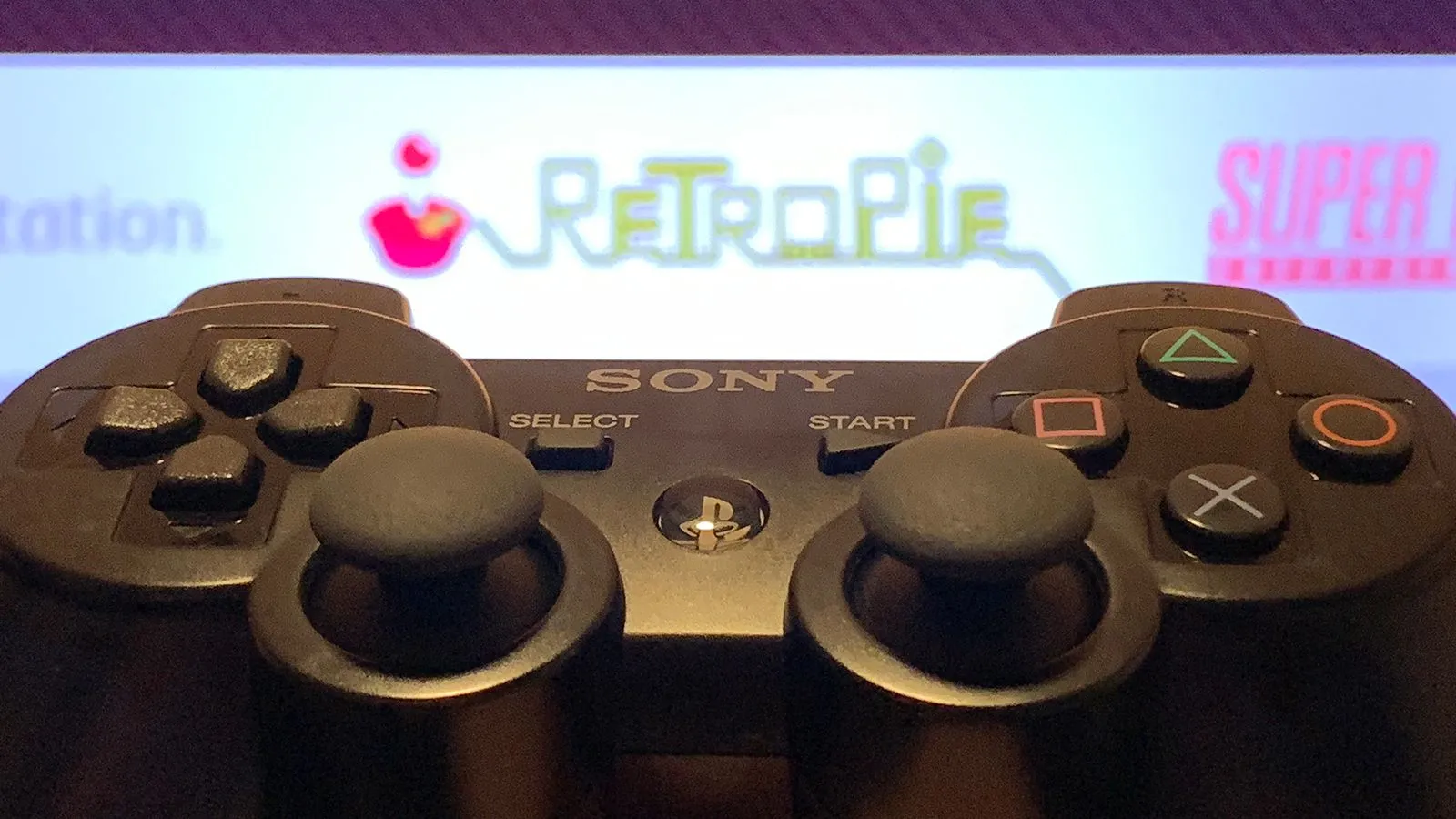 Tay cầm chơi game PS3 với giao diện RetroPie trên màn hình, biểu tượng của máy chơi game retro Raspberry Pi
