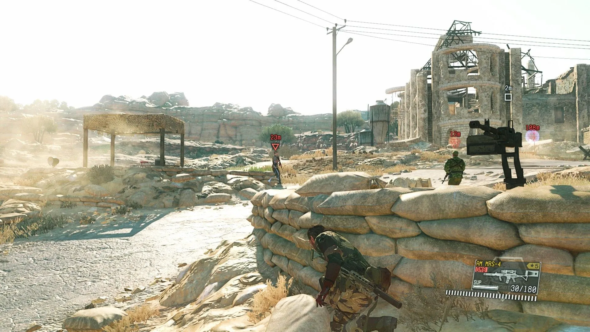 Venom Snake ẩn nấp sau vật cản trong môi trường mở của Metal Gear Solid V The Phantom Pain.